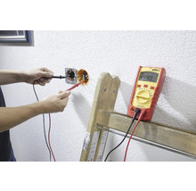 Iemand meet de spanning van een stopcontact met een multimeter.