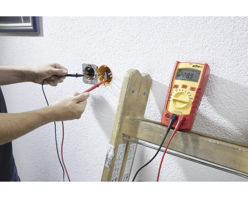 Iemand meet de spanning van een stopcontact met een multimeter.