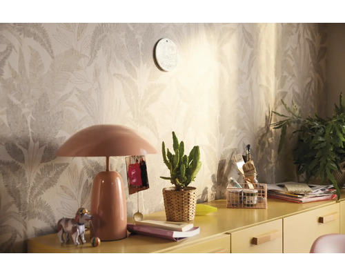 Decoratieve kamer met patroonbehang, tafellamp en diverse decoraties op een gele kast.