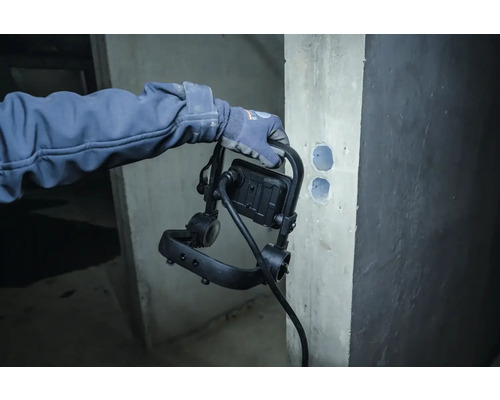 Een persoon houdt een bouwlamp vast, in de buurt van een muur met boorgaten.