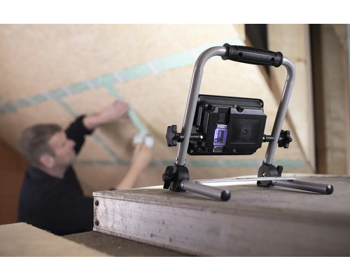 Arbeider onder dak monteert isolatie met bouwlamp