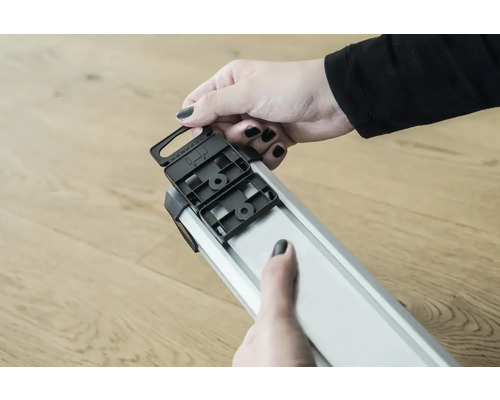 Close-up van een persoon die een zwart kunststof onderdeel aan een zilverkleurig aluminium profiel bevestigt