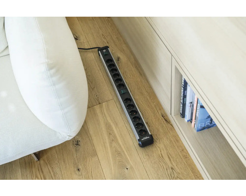 Stekkerdoos met meerdere stopcontacten op houten vloer naast bank en plank