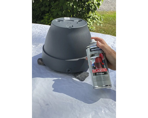 Een persoon spuit een bloempot met kunststofprimer.