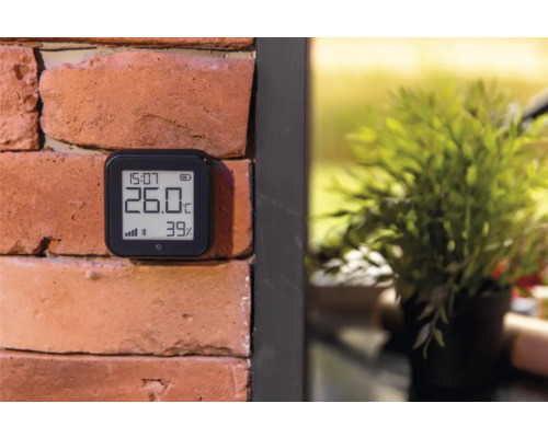 Digitale thermometer op een bakstenen muur voor het weergeven van temperatuur en vochtigheid.