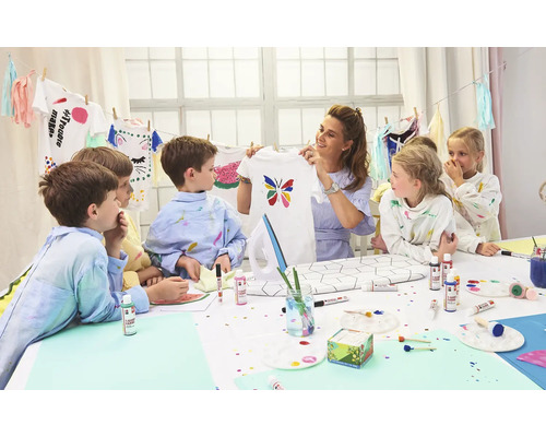 Een groep kinderen en een vrouw versieren T-shirts met textielverf aan een tafel.