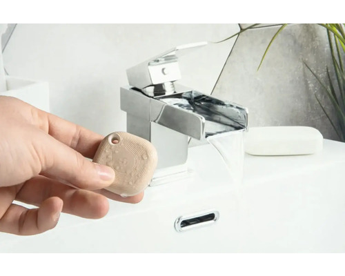 Een persoon houdt een aromasteen vast voor een kraan in de badkamer