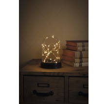 Decoratieve glazen koepel met lichtjes op een nachtkastje naast boeken