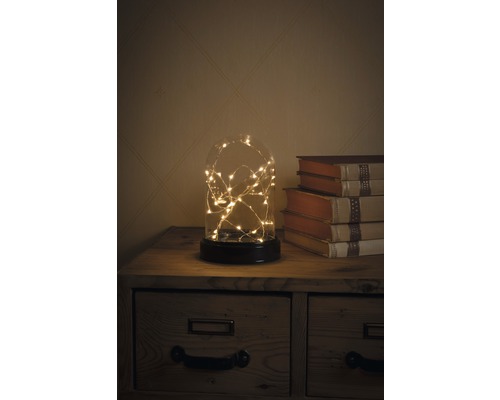 Decoratieve glazen koepel met lichtjes op een nachtkastje naast boeken