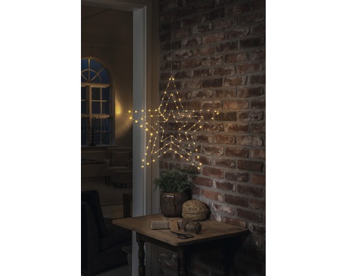 Decoratieve ster met ledverlichting, hangend aan een bakstenen muur boven een klein tafeltje met decoratie.