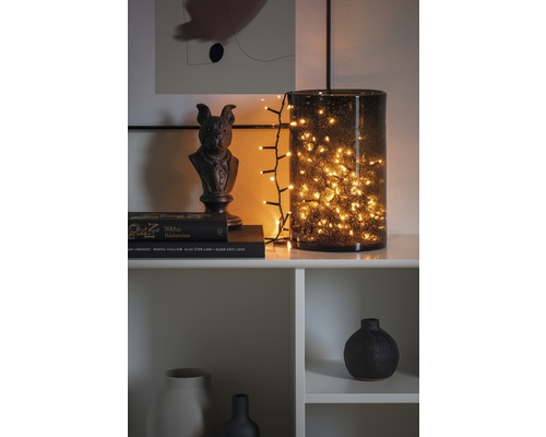 Decoratieve opstelling met lichtslinger in glazen vaas, beeld en boeken op een plank