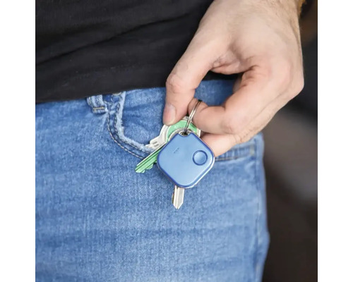 Een hand stopt een sleutelvinder samen met sleutels in een broekzak