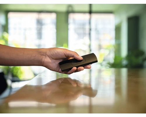 Een hand houdt een zwarte afstandsbediening vast.