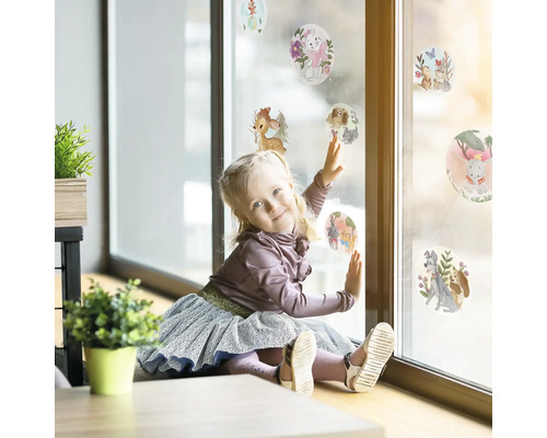 Meisje speelt met raamstickers met diermotieven op een ruit.