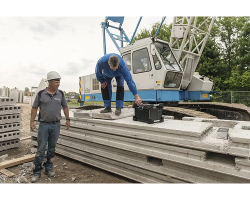 Twee bouwvakkers met bouwplaatsradio en geprefabriceerde betonelementen voor een kraan