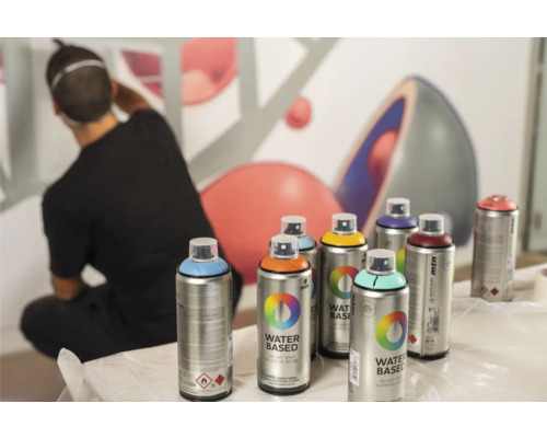 Verschillende Montana verfspuitbussen voor een muur met een man die wegloopt.