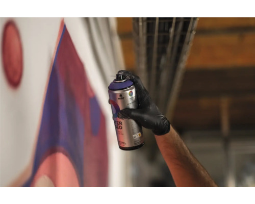 Een persoon spuit met een spuitbus verf op een muur en maakt een graffiti.