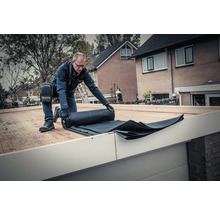 Een man rolt een zwart dakmembraan uit op een dak.