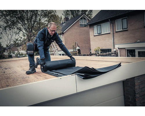 Een man rolt een zwart dakmembraan uit op een dak.