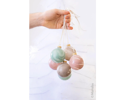 Een hand houdt zes gemarmerde kerstballen aan een touwtje vast.