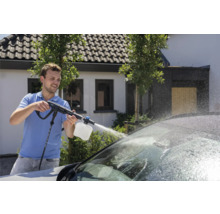 Een man gebruikt een hogedrukreiniger om een auto te wassen.
