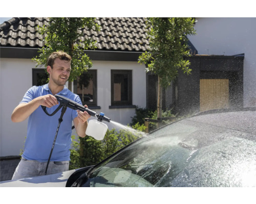 Een man gebruikt een hogedrukreiniger om een auto te wassen.