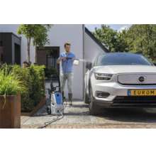 Een man maakt een auto schoon met een hogedrukreiniger buiten.