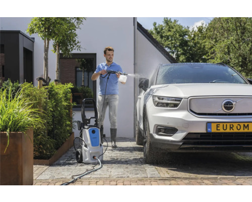 Een man maakt een auto schoon met een hogedrukreiniger buiten.