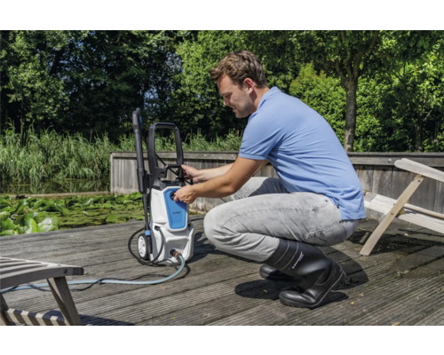 Man bedient een hogedrukreiniger buitenshuis op een houten terras bij een waterpartij