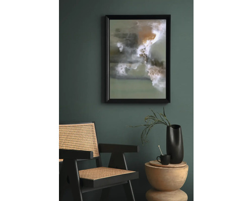 Scène met een ingelijst abstract kunstwerk, een rotan stoel en een bijzettafel met decoratie.