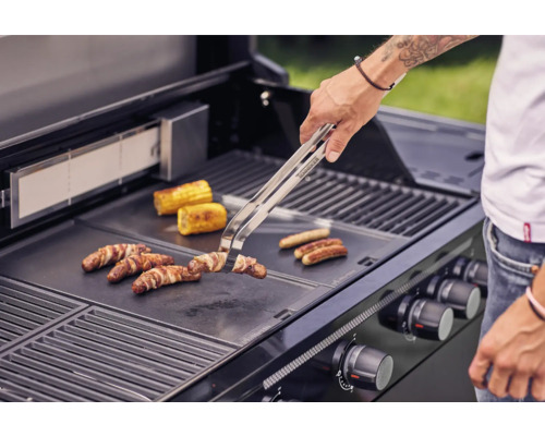 Persoon grilt worstjes, spek en maiskolven op een barbecue.