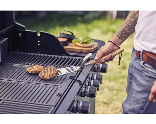 Persoon draait burgers op een grill met een spatel