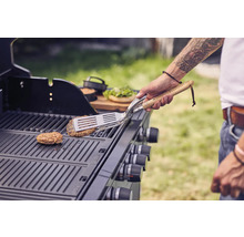 Persoon draait burger om op een gasbarbecue met barbecuegereedschap