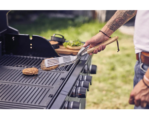 Persoon draait burger om op een gasbarbecue met barbecuegereedschap