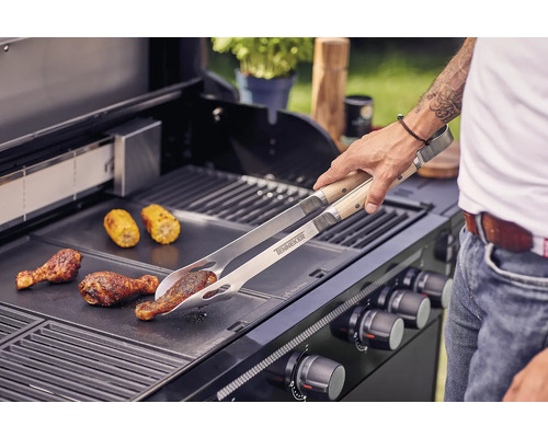 Man grilt kippenpoten en maiskolven met een grilltang op een barbecue