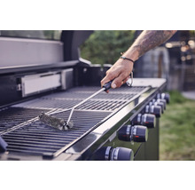 Een persoon reinigt een grillrooster met een grillborstel.