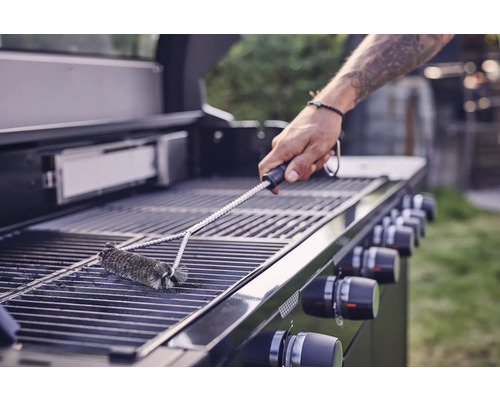Een persoon reinigt een grillrooster met een grillborstel.