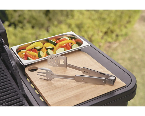 Groenten in een schaal, grilltang en snijplank op een barbecue