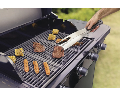Barbecue met gegrilde etenswaren zoals steaks, worstjes en maïskolven, bediend met een tang.