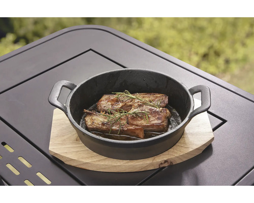 Gegrild vlees met rozemarijn in een zwarte gietijzeren pan op een houten tafel