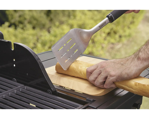 Iemand snijdt een baguette met een grillspatel op een barbecue.