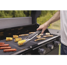 Barbecue met maiskolven, worstjes en knoflook op het rooster en een persoon met een barbecuegereedschap.