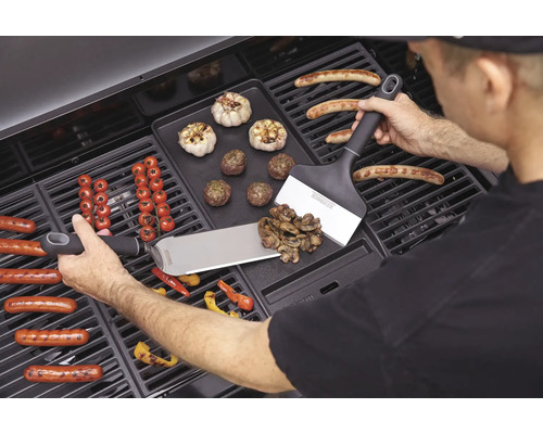 Man grilt worstjes, groenten en knoflook op een barbecue met barbecuespatels.