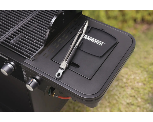 Detailopname van een zwarte gasbarbecue met een grilltang op de zijplank en het Tenneker logo.