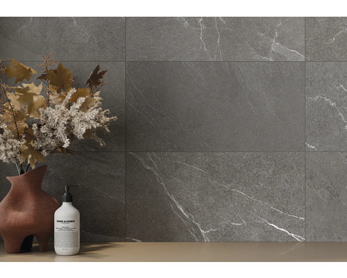 Grijze tegels met marmerlook op een wand, aangevuld met een vaas met bloemdecoratie en een zeepfles