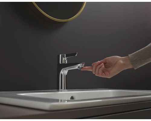 Een hand bedient een metalen kraan op een wastafel.