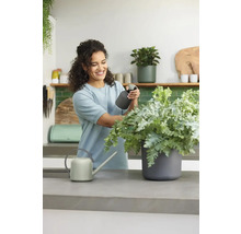 Vrouw verzorgt plant met spuitfles naast gieter op een werkblad