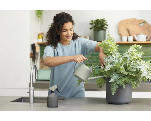Vrouw geeft plant water in de keuken met gieter