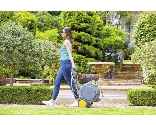 Vrouw trekt een tuinslangwagen in een tuin met fontein.