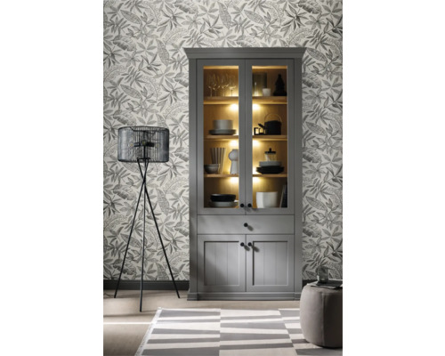 Woonkamer met grijze vitrinekast, staande lamp en behang met print.